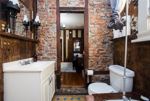 bathroom featuring vanity, toilet, and brick wall