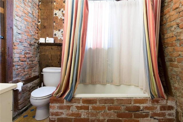 bathroom featuring toilet, shower / bath combo with shower curtain, and brick wall