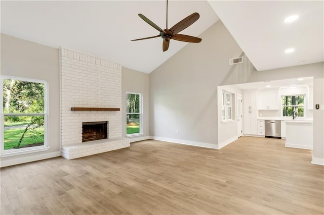 unfurnished living room with plenty of natural light, a fireplace, light hardwood / wood-style floors, and high vaulted ceiling