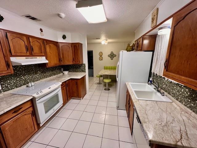 kitchen featuring sink, decorative backsplash, light tile patterned floors, white appliances, and a textured ceiling