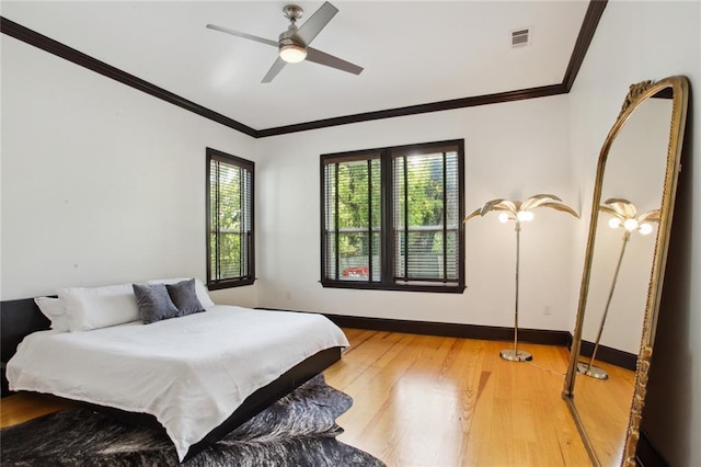 bedroom with light wood finished floors, visible vents, baseboards, and crown molding