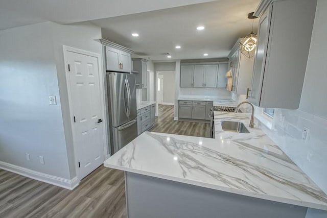 kitchen with sink, hanging light fixtures, dark wood-type flooring, kitchen peninsula, and stainless steel fridge