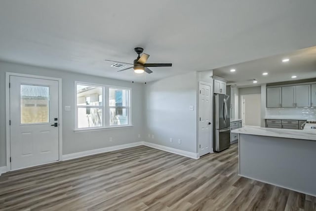 interior space featuring decorative backsplash, ceiling fan, wood-type flooring, gray cabinets, and stainless steel refrigerator