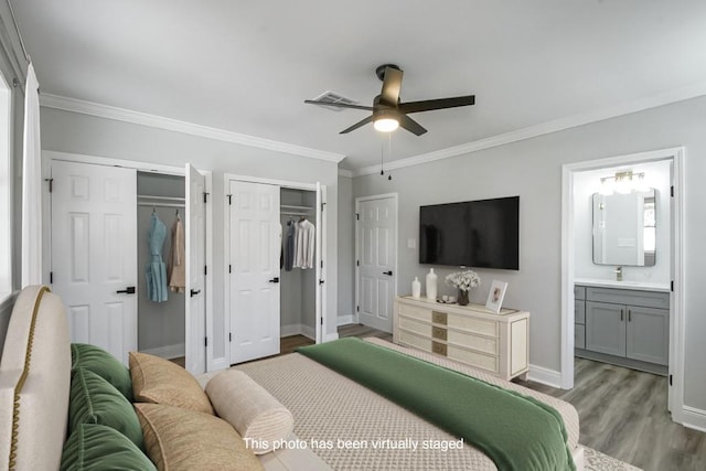 bedroom featuring crown molding, ceiling fan, connected bathroom, wood-type flooring, and multiple closets