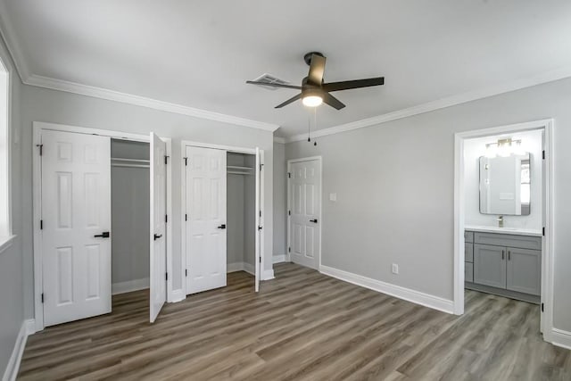 unfurnished bedroom with dark wood-type flooring, ensuite bathroom, crown molding, ceiling fan, and multiple closets