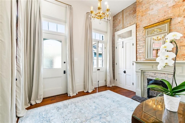 doorway featuring brick wall, a large fireplace, dark wood-type flooring, and a notable chandelier