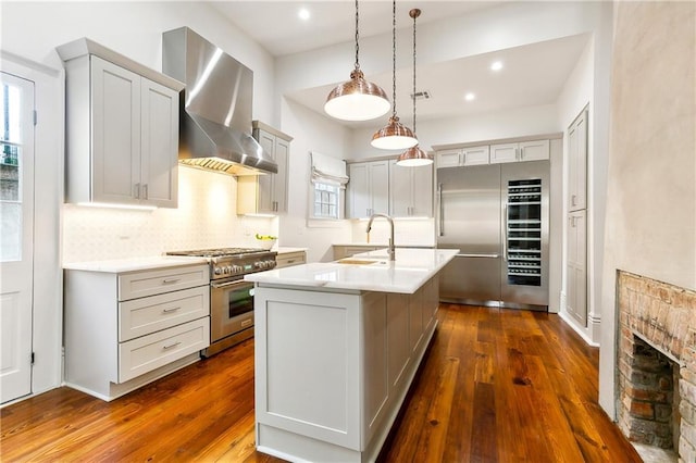 kitchen featuring a center island with sink, hanging light fixtures, wall chimney exhaust hood, decorative backsplash, and premium appliances