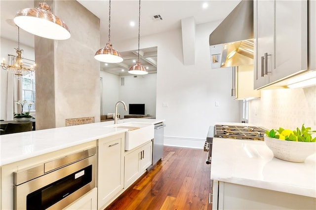 kitchen featuring built in microwave, dark wood-type flooring, sink, pendant lighting, and range hood