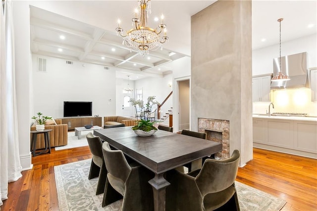 dining space with beamed ceiling, light hardwood / wood-style floors, a fireplace, and coffered ceiling