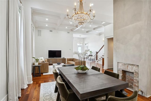 dining area featuring a high end fireplace, coffered ceiling, an inviting chandelier, beamed ceiling, and hardwood / wood-style floors