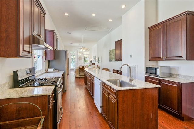 kitchen featuring sink, dark wood-type flooring, stainless steel range with gas cooktop, light stone counters, and a kitchen island with sink