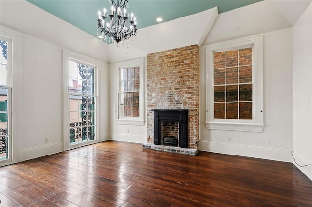 unfurnished living room with an inviting chandelier, lofted ceiling, wood-type flooring, and a fireplace