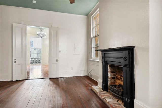 unfurnished living room featuring dark wood-type flooring, crown molding, a chandelier, and a brick fireplace