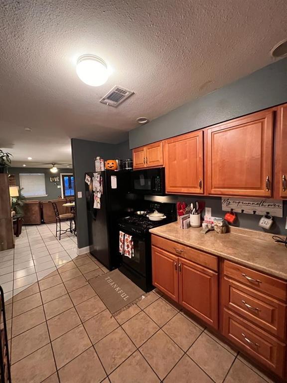 kitchen with light tile patterned floors, black appliances, and a textured ceiling