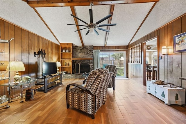 living room with ceiling fan, built in features, lofted ceiling with beams, a textured ceiling, and a fireplace