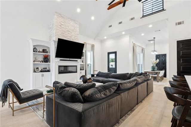 living room featuring ceiling fan, a stone fireplace, built in features, high vaulted ceiling, and light hardwood / wood-style floors