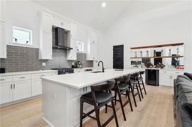 kitchen featuring white cabinetry, stainless steel range, wall chimney range hood, an island with sink, and a breakfast bar area