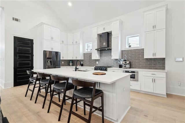 kitchen with sink, wall chimney exhaust hood, a kitchen island with sink, a breakfast bar, and appliances with stainless steel finishes