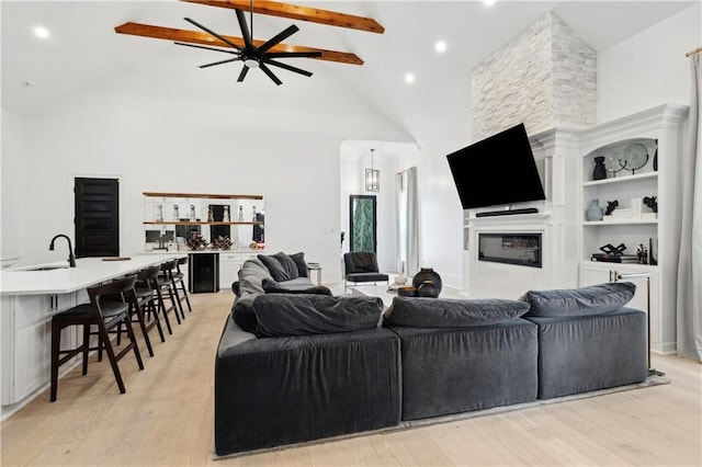 living room with ceiling fan, sink, a stone fireplace, built in features, and light wood-type flooring