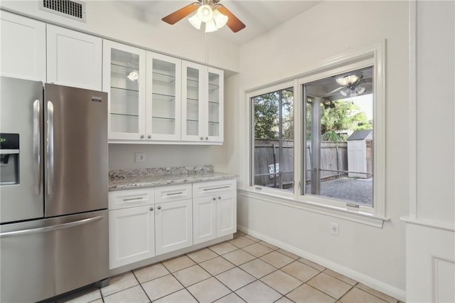 kitchen featuring light stone countertops, stainless steel fridge, ceiling fan, light tile patterned floors, and white cabinets