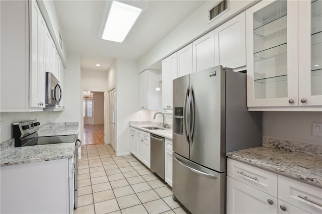 kitchen with appliances with stainless steel finishes, light tile patterned floors, white cabinetry, and sink