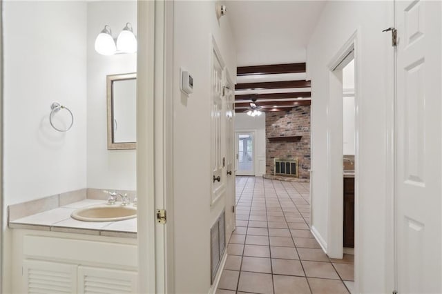 bathroom featuring a brick fireplace, vanity, ceiling fan, beamed ceiling, and tile patterned flooring