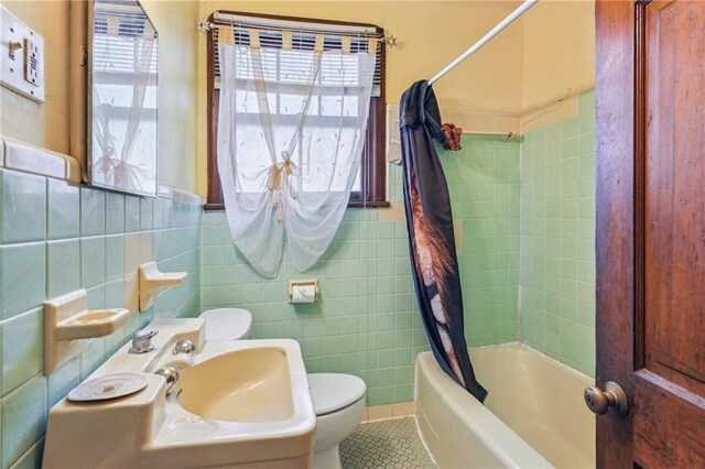 full bathroom with a healthy amount of sunlight, toilet, shower / bath combo with shower curtain, and tile walls