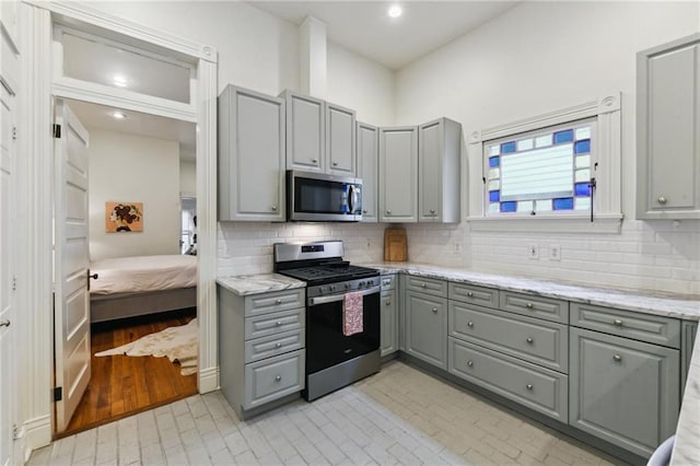 kitchen with tasteful backsplash, gray cabinets, light stone counters, and stainless steel appliances