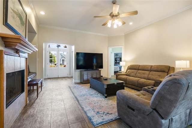 living room featuring dark hardwood / wood-style floors, ceiling fan, ornamental molding, and a tiled fireplace