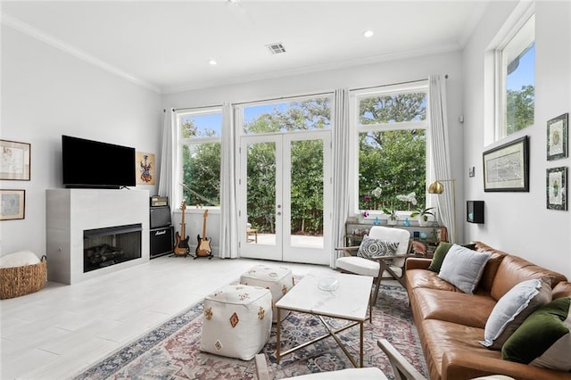 living room with plenty of natural light, crown molding, a tile fireplace, and french doors