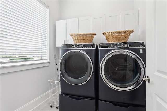 clothes washing area featuring cabinets, light tile patterned floors, and washer and clothes dryer