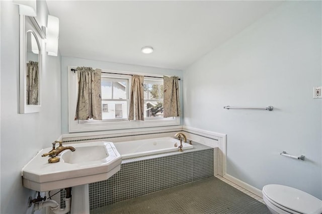 bathroom featuring toilet, a relaxing tiled tub, and tile patterned floors