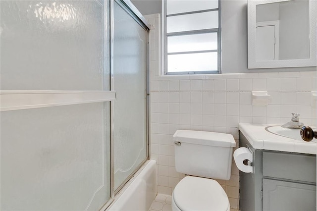 full bathroom featuring vanity, toilet, shower / bath combination with glass door, and tile walls