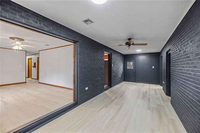 unfurnished room with ceiling fan, brick wall, a textured ceiling, and light hardwood / wood-style floors