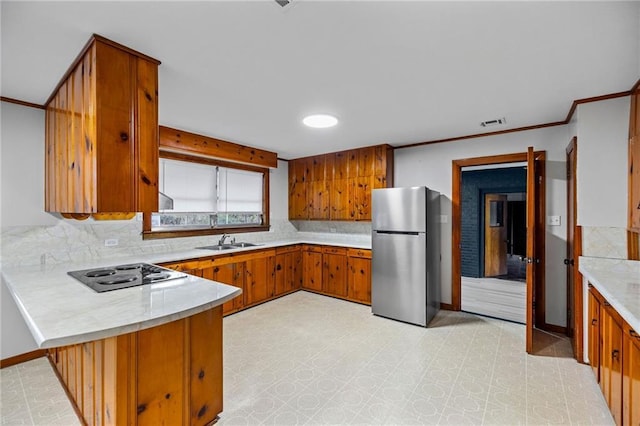 kitchen featuring kitchen peninsula, tasteful backsplash, gas stovetop, sink, and stainless steel refrigerator