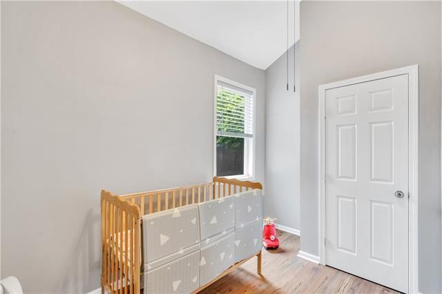 bedroom with lofted ceiling, a crib, and light hardwood / wood-style flooring