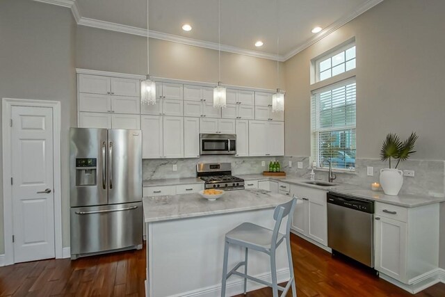 kitchen with appliances with stainless steel finishes, white cabinets, decorative light fixtures, crown molding, and sink