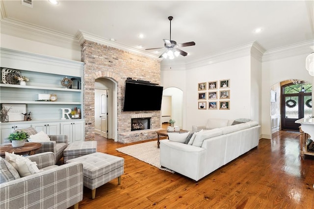 living room featuring hardwood / wood-style flooring, ceiling fan, a stone fireplace, and built in features