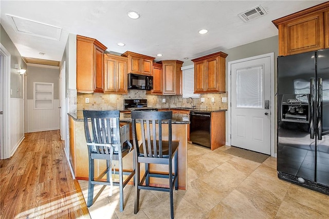 kitchen with black appliances, sink, dark stone countertops, a kitchen island, and a kitchen bar