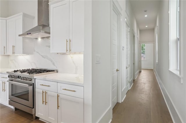 kitchen featuring decorative backsplash, light stone countertops, wall chimney range hood, high end stainless steel range, and white cabinets