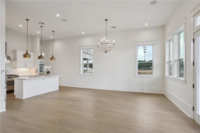 kitchen featuring pendant lighting, a kitchen island with sink, white cabinets, stainless steel stove, and light wood-type flooring