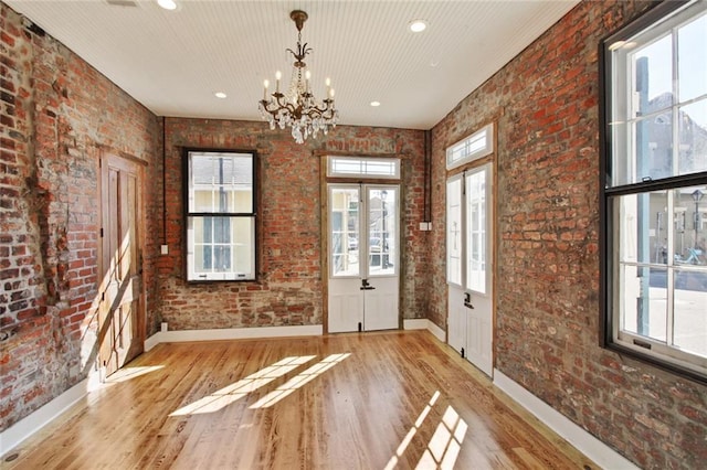 doorway to outside featuring light hardwood / wood-style flooring, an inviting chandelier, a wealth of natural light, and brick wall