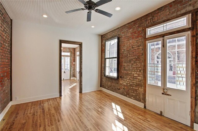 spare room featuring ceiling fan, light hardwood / wood-style flooring, and brick wall