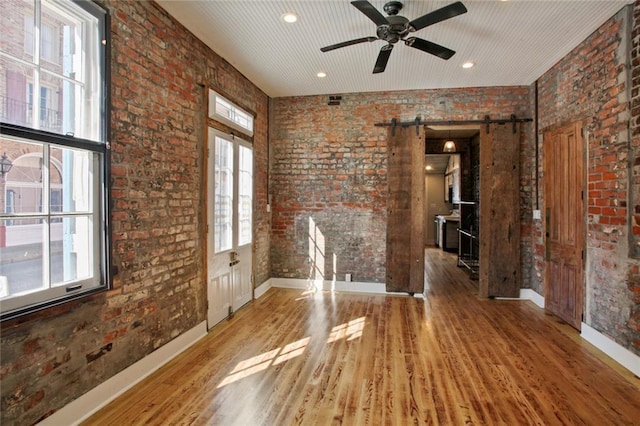 interior space featuring a barn door, hardwood / wood-style floors, a healthy amount of sunlight, and brick wall