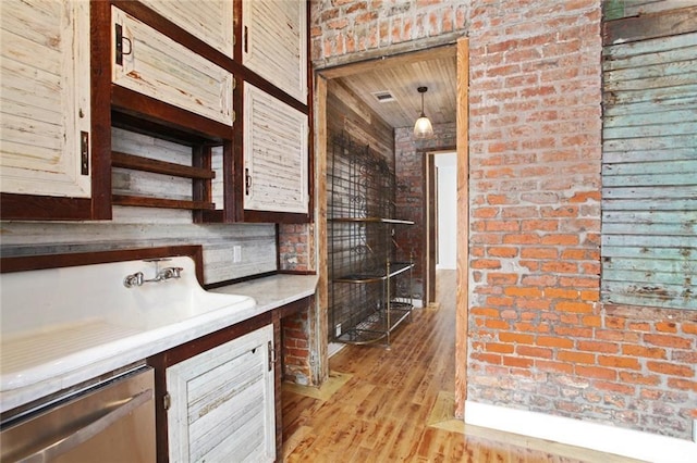 bar with pendant lighting, sink, stainless steel dishwasher, light hardwood / wood-style floors, and brick wall