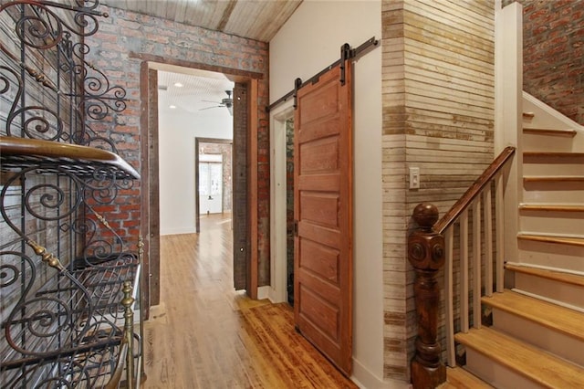 corridor featuring light wood finished floors, brick wall, a barn door, and stairway