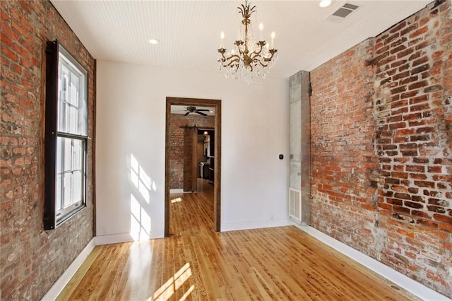 spare room featuring brick wall, light wood-type flooring, visible vents, and baseboards