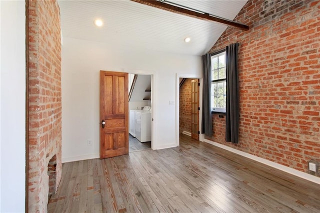 spare room featuring vaulted ceiling with beams, brick wall, wood finished floors, baseboards, and washer and dryer