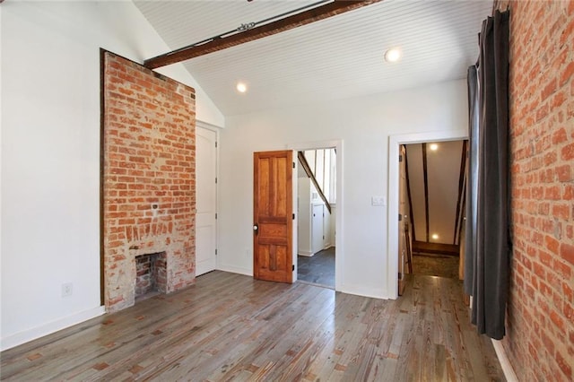 unfurnished living room with hardwood / wood-style flooring, lofted ceiling with beams, a fireplace, and brick wall