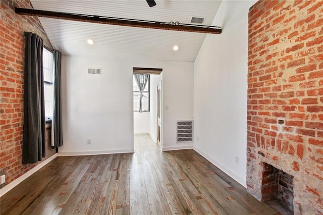 spare room with hardwood / wood-style flooring, lofted ceiling with beams, brick wall, and a wealth of natural light